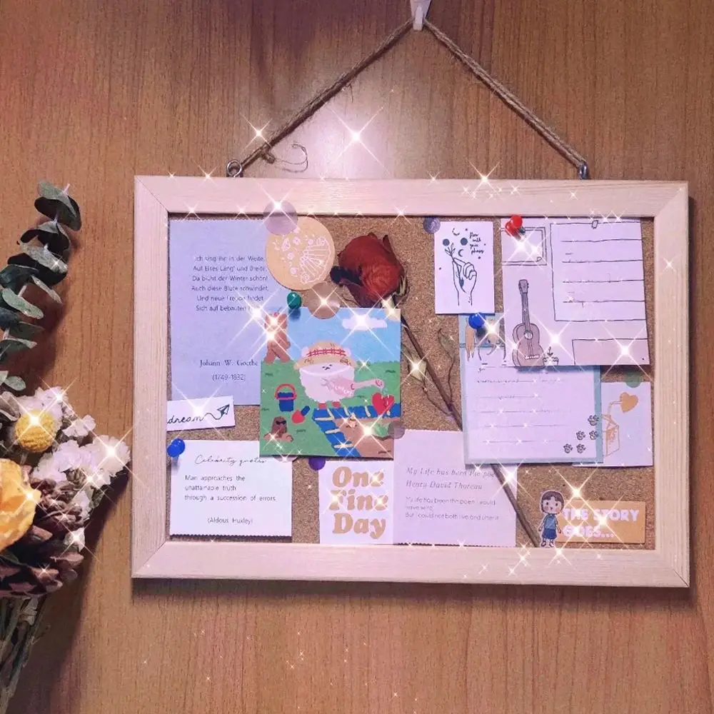 S221d3ee5597f4e299b9ebfd8192a87c2t.webp Prikbord van kurk met lichte houten lijst aan de muur met vastgeprikte notities en foto's