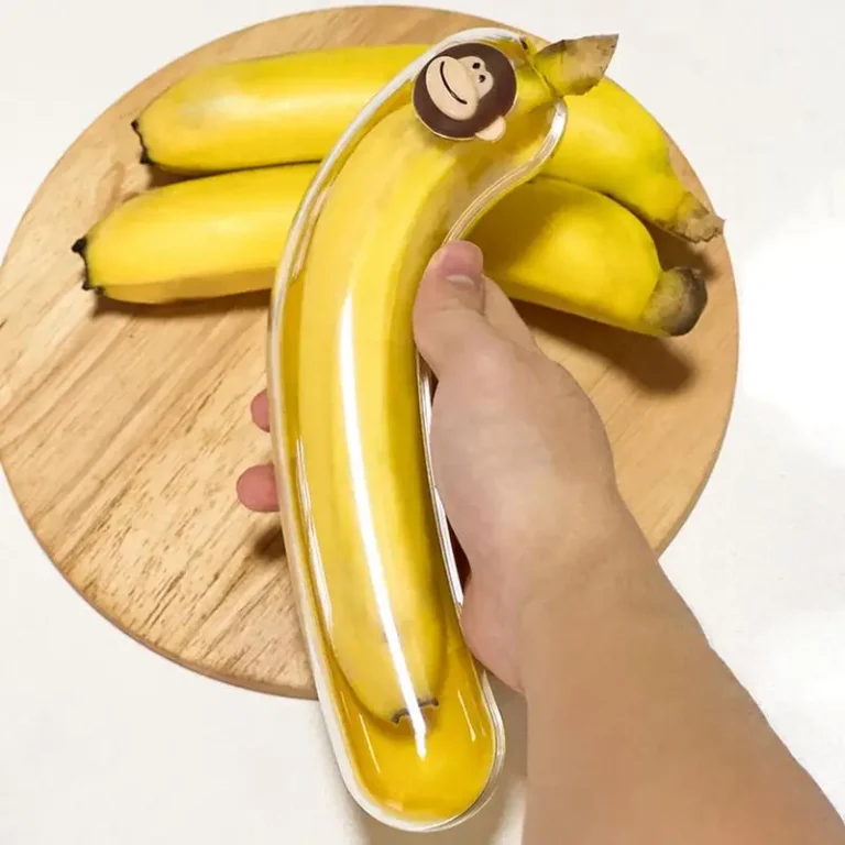 Transparante bananendoos met apenkapje boven bananen op een houten plank