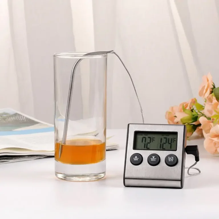 Digitale thermometer met sonde in een glas op een tafel met bloemen