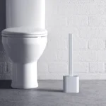 Witte siliconen toiletborstel in houder op een badkamervloer naast het toilet
