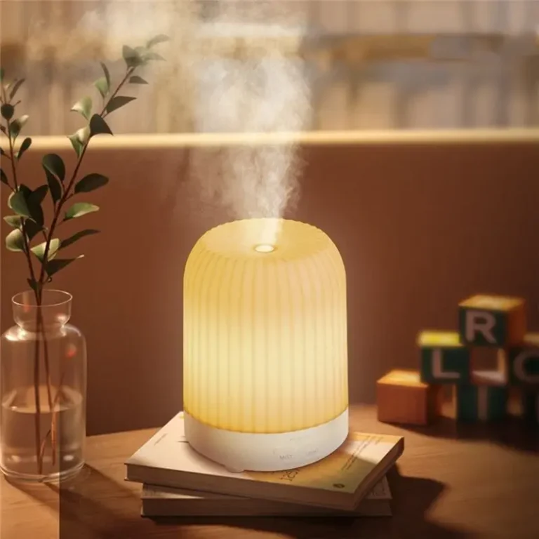 Verlichte aromadiffuser die nevel verspreidt op een stapel boeken naast een vaas