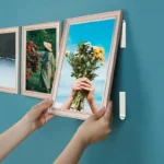 Handen hangen een fotolijst aan een petrolkleurige muur met witte plakstrips