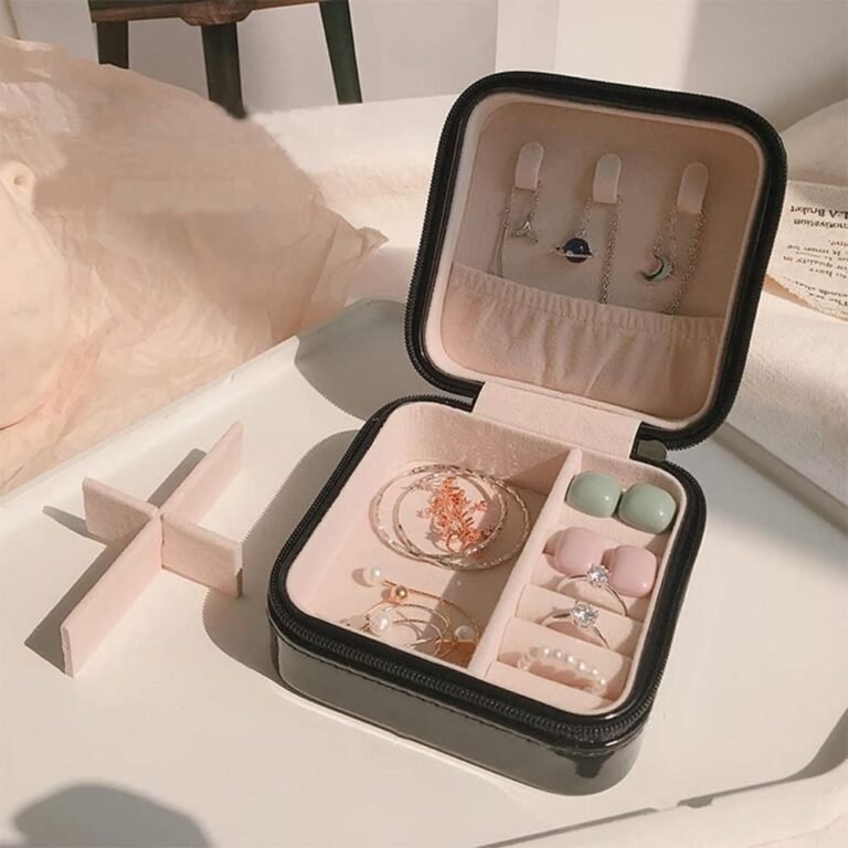 Open zwart reissieradendoosje met ringen en oorbellen op een wit dienblad in een slaapkamer